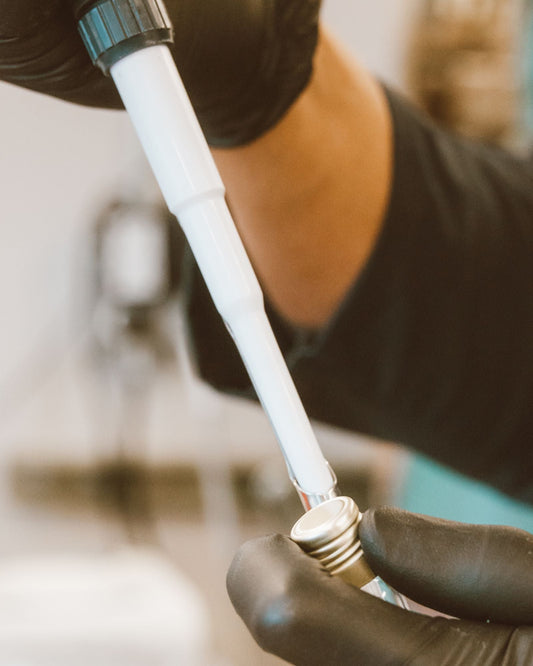 Detalhe de mãos com luvas utilizando pipeta e pequeno frasco em atividade de laboratório